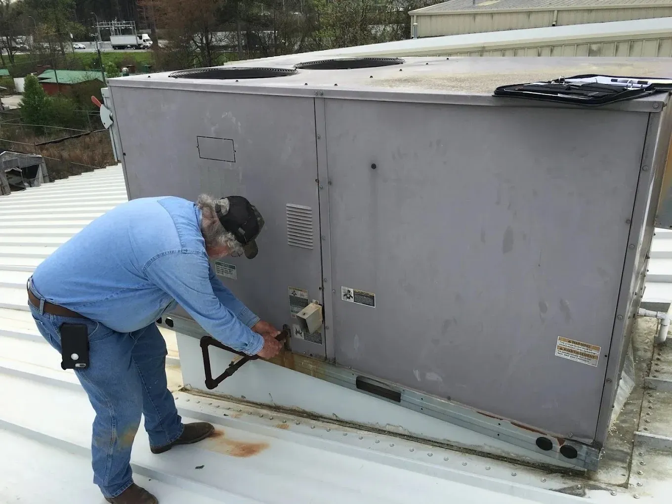 The One Call Heating & Cooling Blog Technician adjusting an HVAC unit on a rooftop.